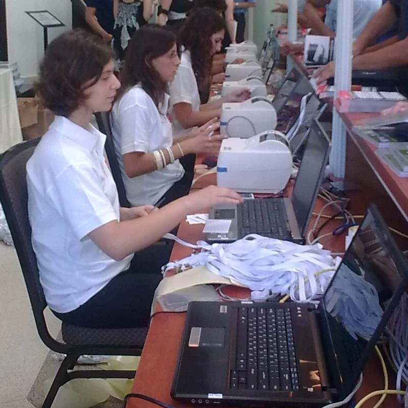 A row of staffed registration desks at an exhibition: hosts at laptops, label printers and badges ready to hand out